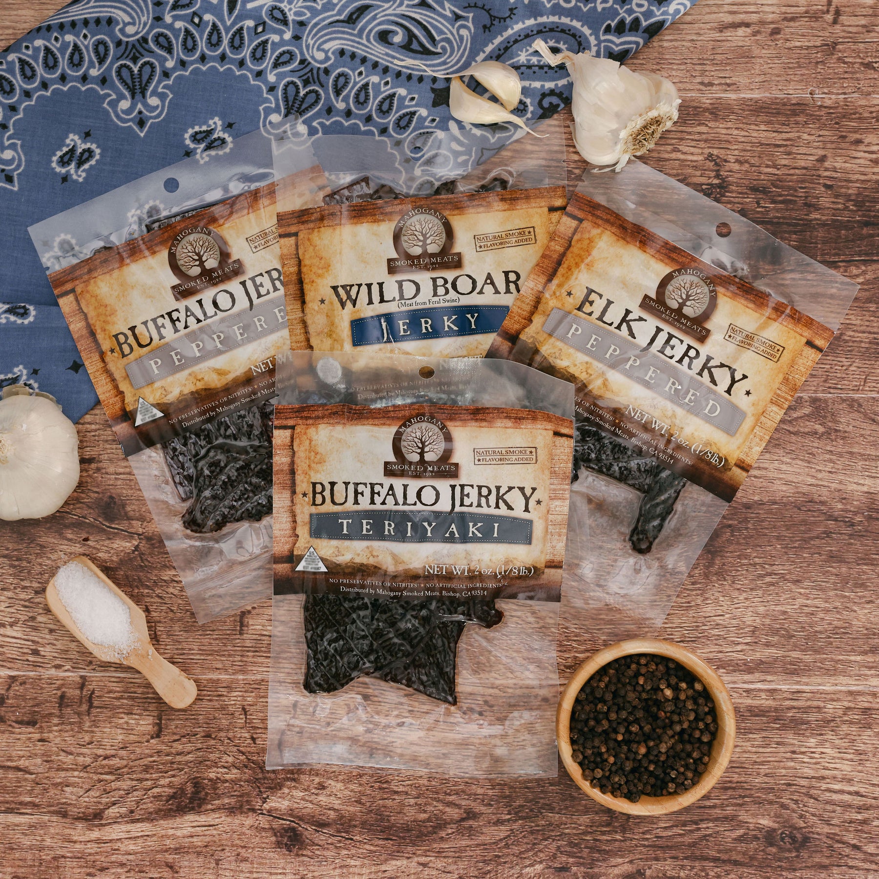 Assorted exotic jerky packets including buffalo, wild boar, and elk on a wooden surface with spices.